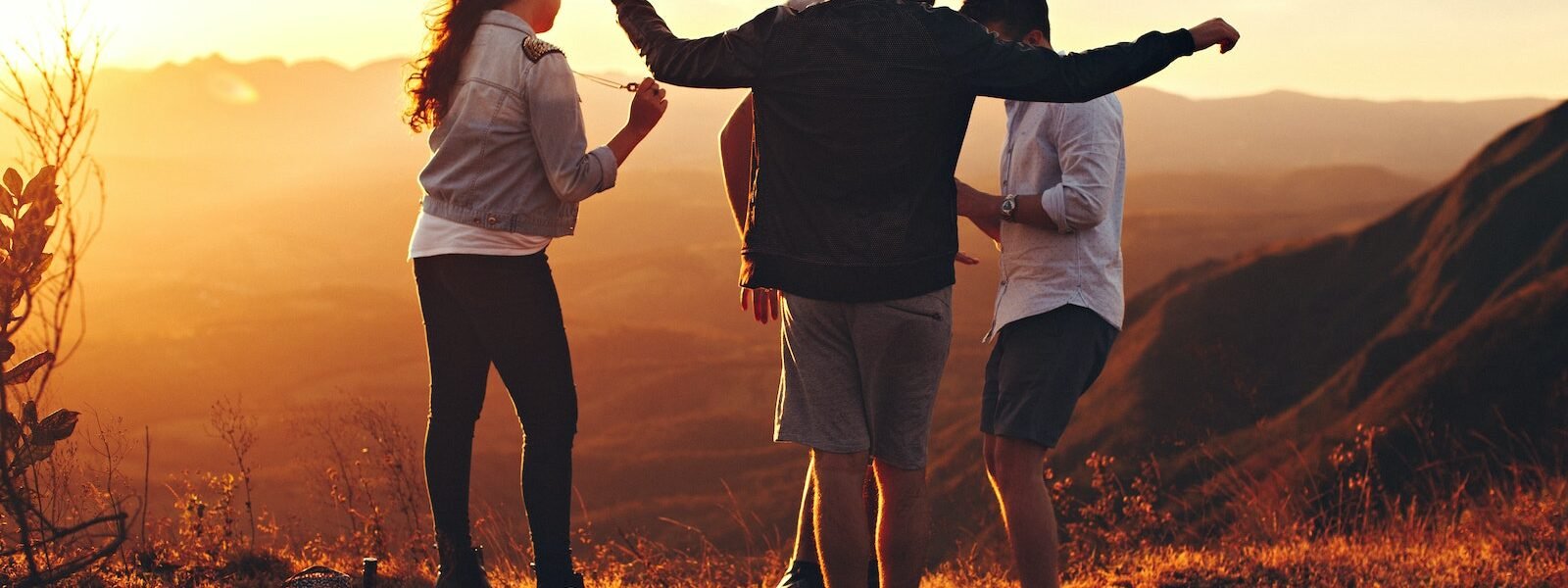 Four Person Standing at Top of Grassy Mountain