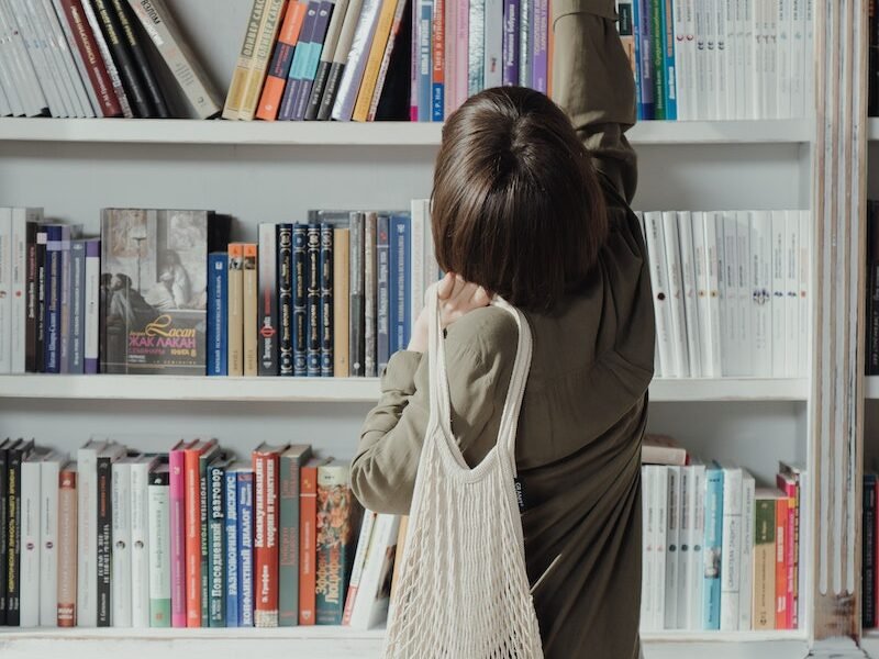 Woman in Beige Long Sleeve Dress Standing in Front of White Wooden Book Shelf