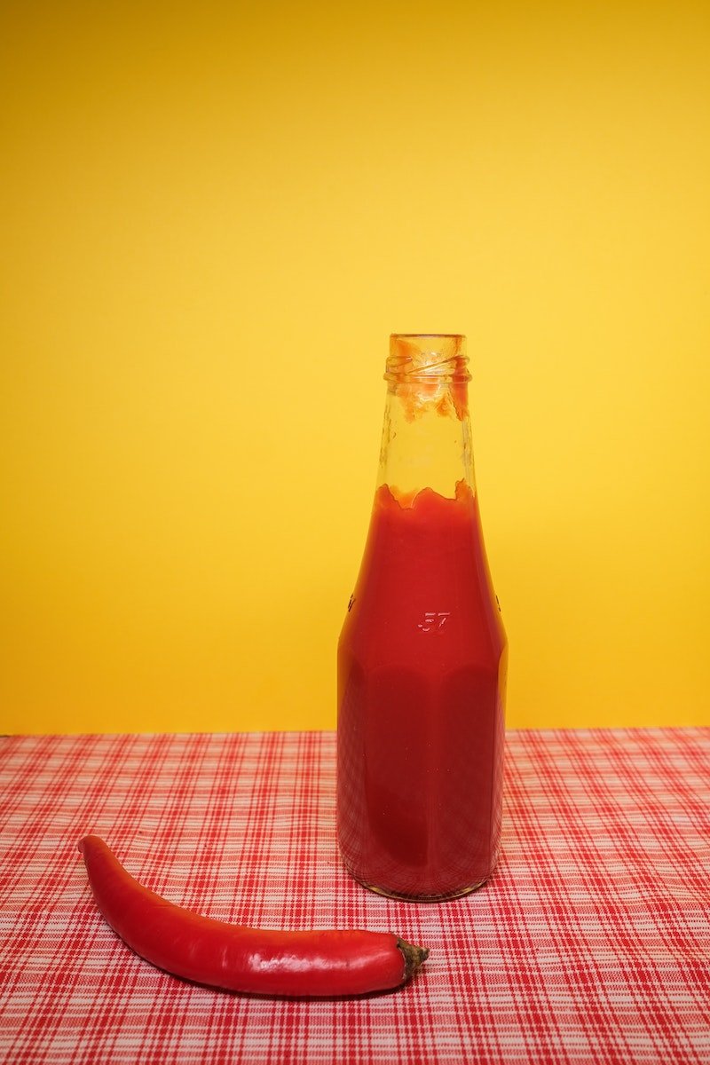 Bottle with ketchup near red chili pepper on table