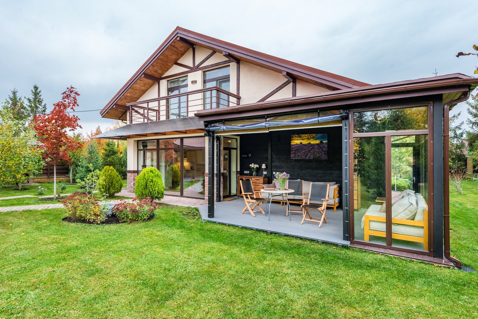 Residential cottage with balcony and opened veranda opening view on lawn and trees growing in backyard