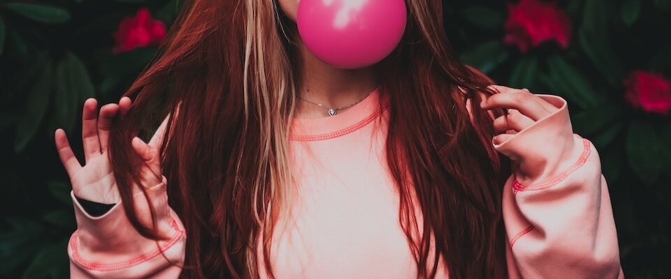 Dreamy woman in trendy clothes blowing pink gum in garden