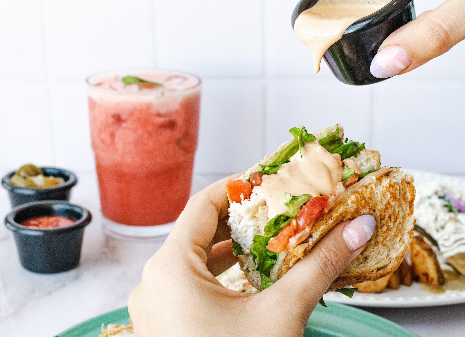 a person pouring dressing on a sandwich on a plate