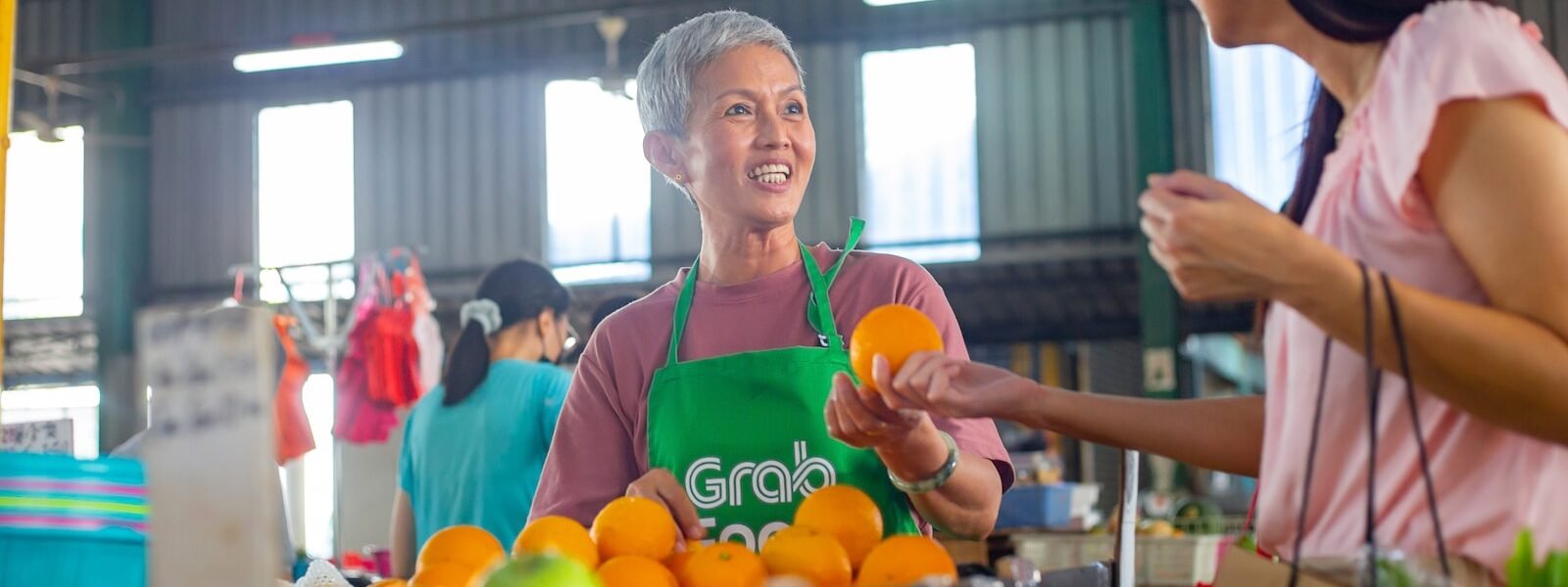 a woman in a green apron standing in front of a table filled with oranges