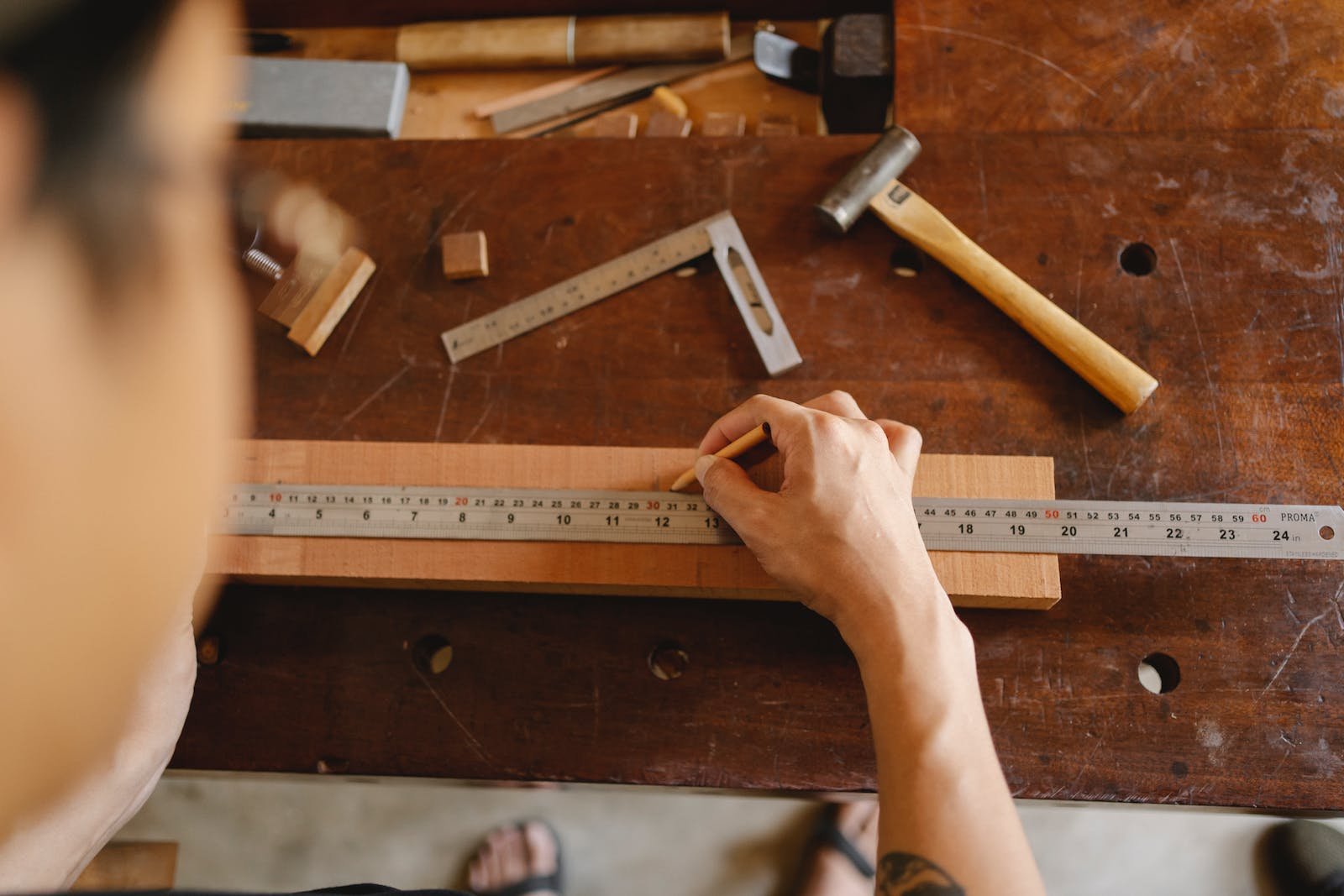 Top view of crop anonymous male measuring timber plank with ruler and marking with pencil while working on table with tools