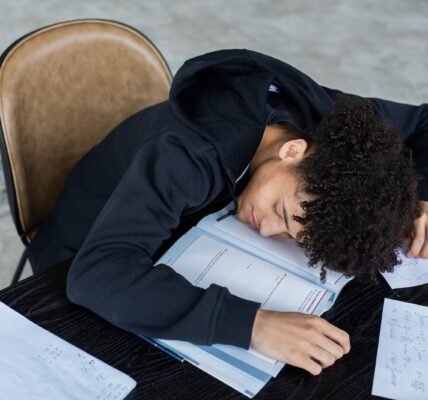 High angle of exhausted African American student resting on opened textbook and papers while preparing for exam